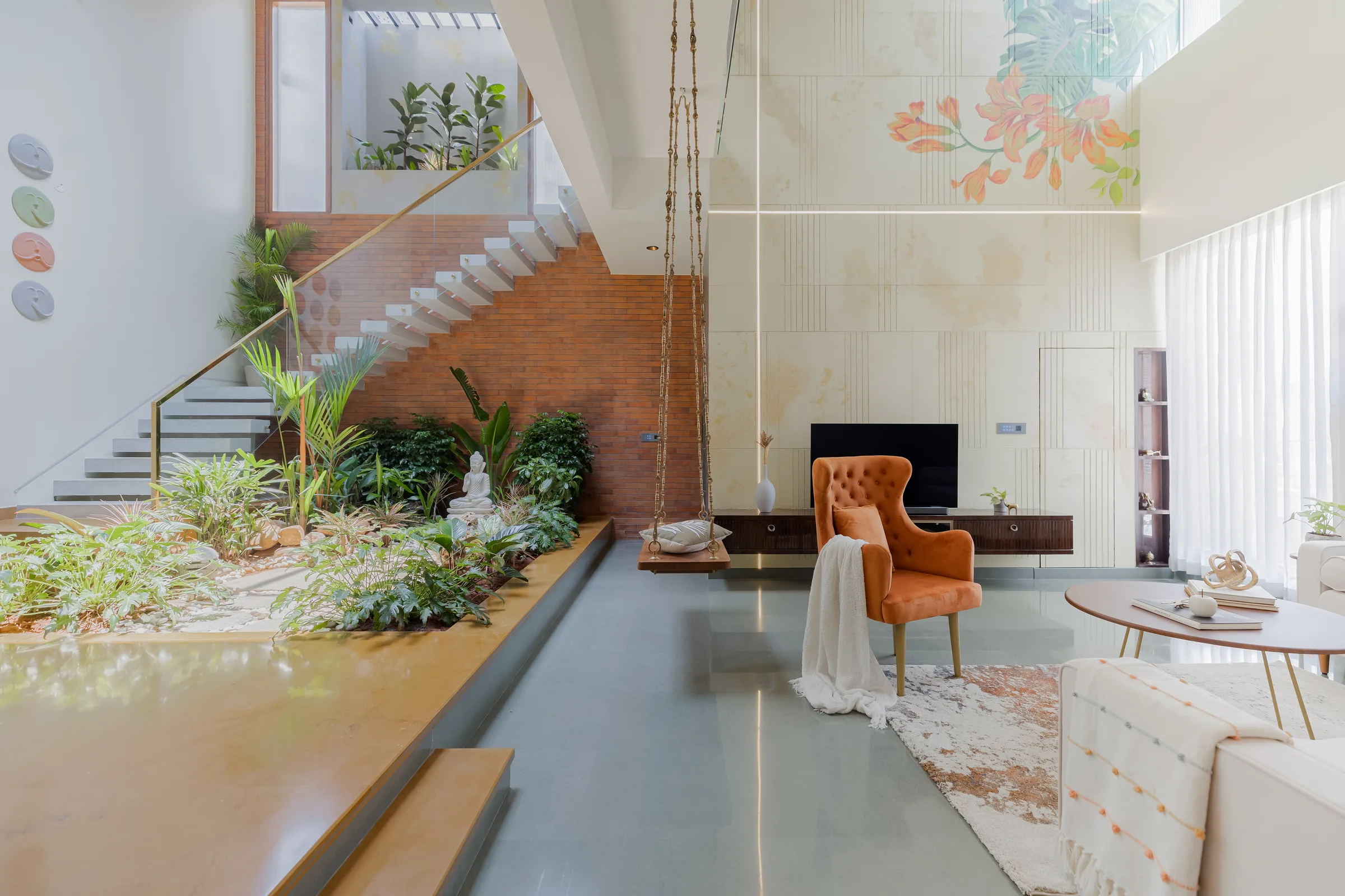 Double-height living room with a swing, indoor planting and a staircase at Madhura Maanasa