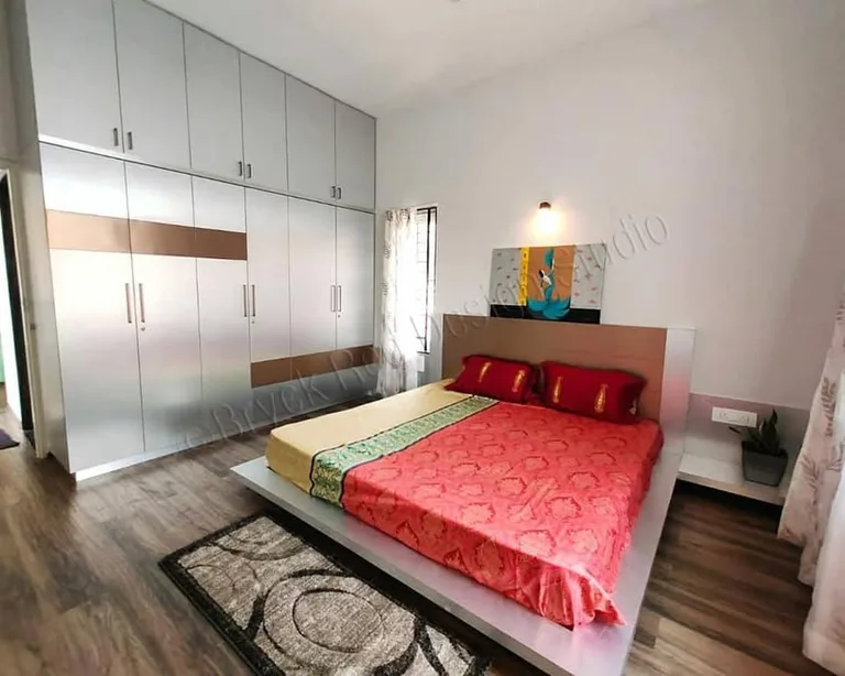 Dharwad bedroom with a red bedspread, full-height white wardrobes and wood-toned flooring
