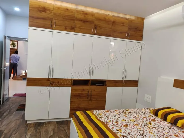 Full-height white bedroom wardrobes framed by warm wood-toned panels in Dharwad